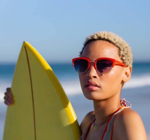 a woman in sunglasses holding a surfboard on the beach