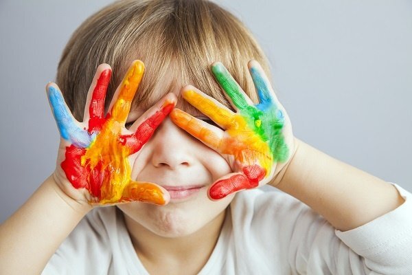 A young boy with colorful paint all over his hands.