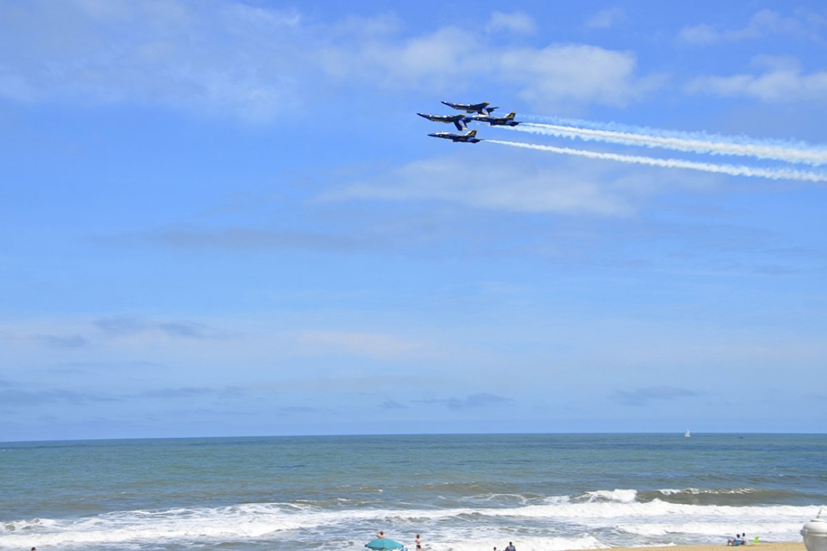 two airplanes flying over the ocean with people watching