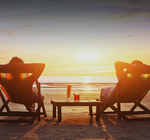 two people sitting in lawn chairs on the beach at sunset